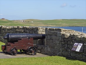 A cannon behind a wall with information sign and sea in the background, old cannons on a stone wall