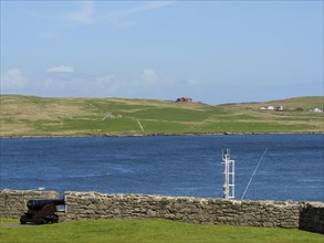 Old cannon in front of a stone wall with a view of the sea and green hills under a blue sky, old