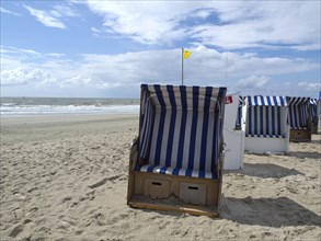 A single blue and white beach chair stands on the beach under a partly cloudy sky, blue and white