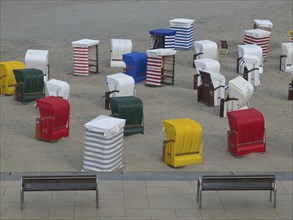 Several colourful beach chairs standing in groups on the sandy beach under a cloudy sky, beach