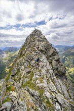 Mountaineer on a narrow mountain path, rocky pointed summit of the Raudenspitze or Monte Fleons,