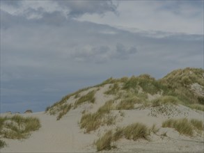 High sand dunes with grass under a sky with clouds, dunes on an island with a blue boat and a