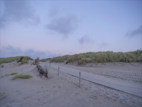 A quiet beach with dunes, sandy path and a simple fence under a clear sky, setting sun on a beach