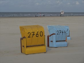 A yellow and a blue beach chair stand close to each other with a view of the sea, colourful beach