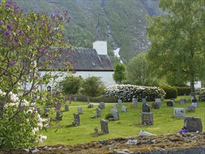 Blooming churchyard with gravestones, green trees and mountains in the background, gravestones with