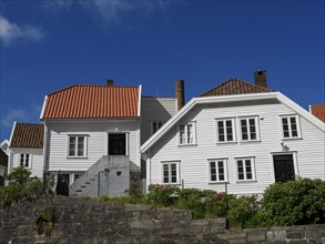 White wooden houses with tiled roofs and chimneys, stone wall in the foreground, sunny day, white