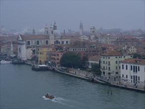 A foggy city view of Venice with historic buildings and boats on the canal, church towers and
