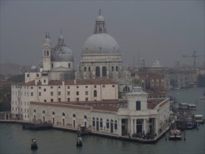 Basilica in Venice next to the water in a foggy atmosphere, with boats and historical buildings,