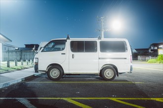 White van parked at night under artificial light with stars in the sky