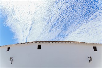 White facade of a bullring with a blue sky with clouds