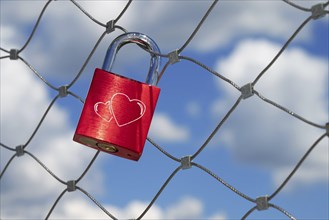 A single red love lock with two engraved hearts hangs from a bridge railing over the Danube,