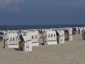 Beach with several numbered beach chairs and sea in the background, dunes and beach at the sea with