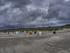 Beach chairs scattered on the dark beach under a dramatically cloudy sky, colourful beach chairs on