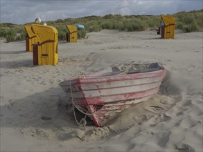 An abandoned boat half sunk in the sand, surrounded by beach chairs and dunes, colourful beach