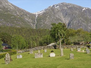 Cemetery with numerous graves on a green meadow in front of an impressive mountain landscape,