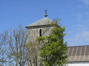 Stone church tower next to green trees, under a clear blue sky, old stone church and many