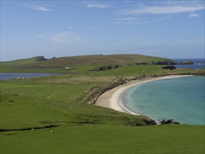 An idyllic coastal scene with rolling green hills, a long sandy beach and calm blue waters under a