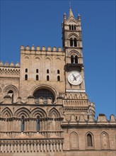Close-up of a cathedral tower with a large clock, under a bright blue sky, two red towers in front