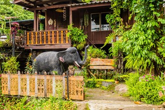 Statue of gray elephant with light blub hanging from trunk standing in front of homestay facility
