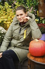 Smiling mid-aged woman in warm down jacket among autumn decoration