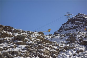 A cable car leads over snow-covered rocks under a clear blue sky, snow on high mountains in the