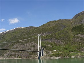 Wide angle view of a bridge over green mountain slopes and forests under a clear blue sky, bridge