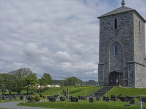 Stone church and cemetery with numerous gravestones under a cloudy sky in a rural setting, old