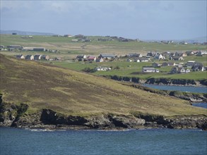 View of a coastal village with several houses on green fields, green meadows on a deep blue sea and