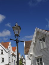 Street lamp in front of white houses with red roofs under blue sky with clouds, white wooden houses