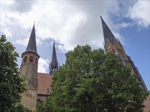 Church spires rising above brick houses and trees into the cloudy sky, large church towers with