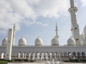 Impressive mosque with several white domes and a high minaret under a partly cloudy sky, beautiful