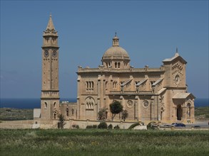Magnificent neo-Romanesque basilica with high bell tower in a vast landscape under a blue sky,