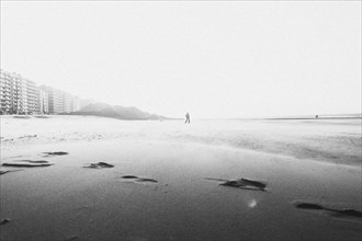 Lonely figure on an empty beach in black and white with the sea in the background. Middelkerke,