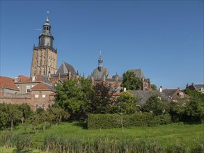 Historic church with a bell tower, surrounded by brick buildings and a green park under a clear