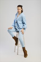 Serious woman in blue knitted suit sits on tall chair