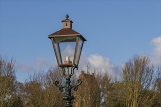 Classic street lamp against a clear blue sky and bare trees in the background, old houses and small