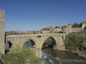 Historic stone bridge over a river surrounded by a city and nature, blue sky in the background,