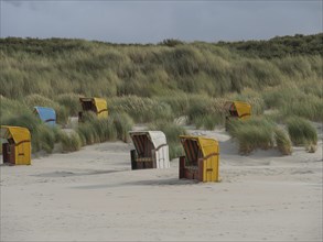 Several beach chairs scattered in front of high dunes under cloudy sky, colourful beach chairs on