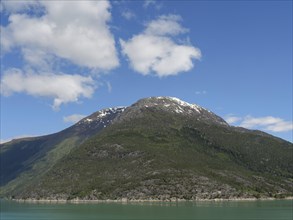Majestic mountain with snow-covered peak and lake below under a clear sky, greenish shimmering