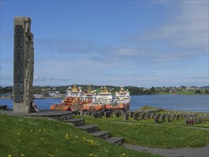 Stone memorial in a cemetery with a view of the harbour and several anchored ships, old stone