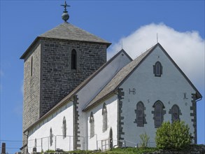 White church with stone tower in close-up, blue sky with some clouds, old stone church and many