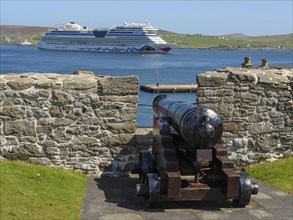 A cannon aims at a large ship in the sea behind a wall, old cannons on a stone wall by the sea