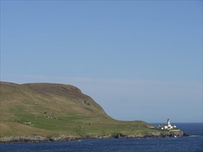 Hilly landscape with a lighthouse by the sea under a blue sky, white lighthouse, on a rocky ground