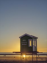 Romantic sunset on the beach of Langeoog with a small green hut in the foreground, beautiful sunset