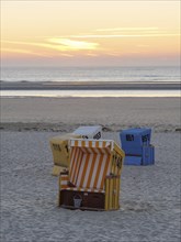 Single colourful beach chairs scattered on the sandy beach during sunset, Sunset on a quiet beach