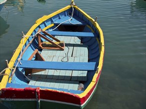 A colourful wooden boat lies quietly on the water in the harbour, many colourful fishing boats in a