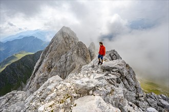 Mountaineer on a rocky narrow summit ridge, cloudy mountain peak, summit of the Great Kinigat,