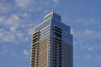 A modern skyscraper with glass facade in front of a clear blue sky with a few clouds, skyline of a
