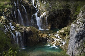 A picturesque waterfall that pours over rocks into crystal-clear water, surrounded by lush green