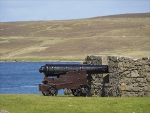 Historic cannon in front of a stone wall with sea view and a hill in the background, old cannons on